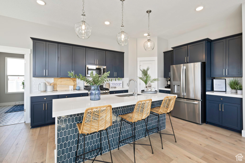 Kitchen with decorative light fixtures, backsplash, light hardwood / wood-style flooring, and stainless steel appliances