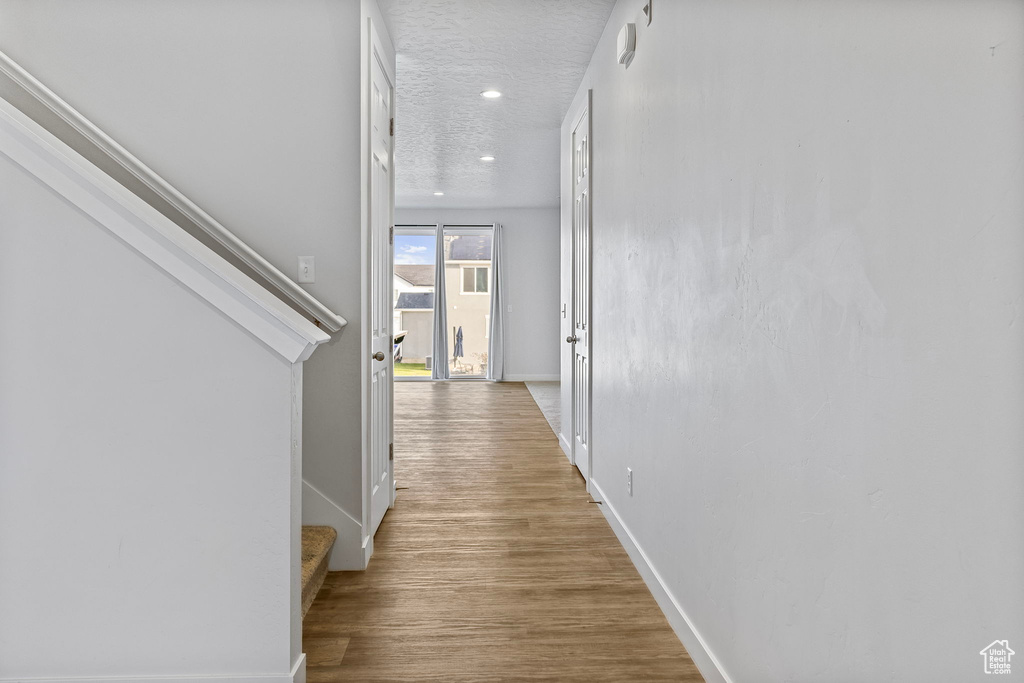 Hallway with a textured ceiling and light hardwood / wood-style flooring