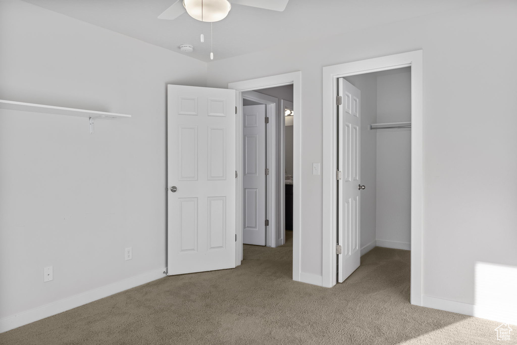 Unfurnished bedroom with ceiling fan, a walk in closet, light colored carpet, and a closet