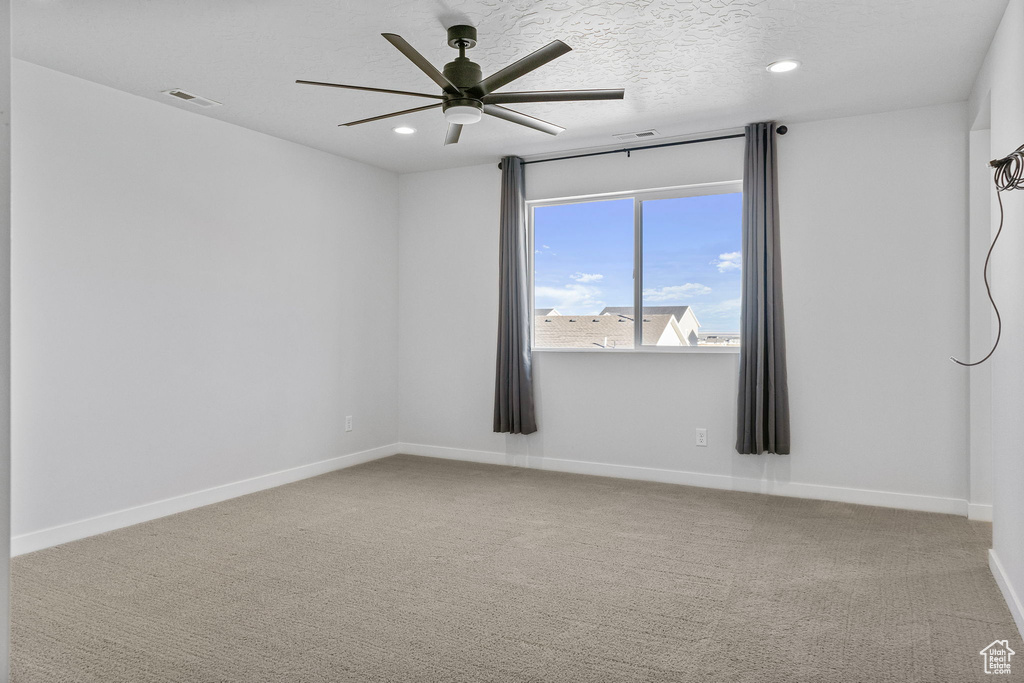 Empty room with light colored carpet, a textured ceiling, and ceiling fan