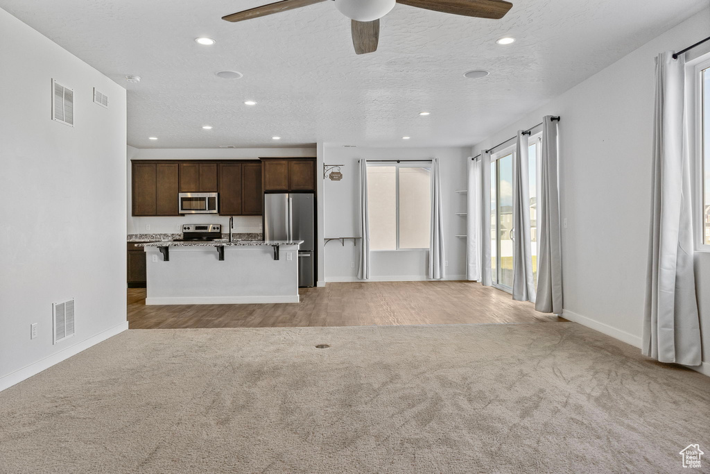 Kitchen featuring stainless steel appliances, light colored carpet, ceiling fan, a breakfast bar area, and a center island with sink