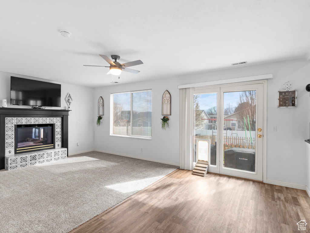 Unfurnished living room featuring ceiling fan, a wealth of natural light, light carpet, and a tiled fireplace
