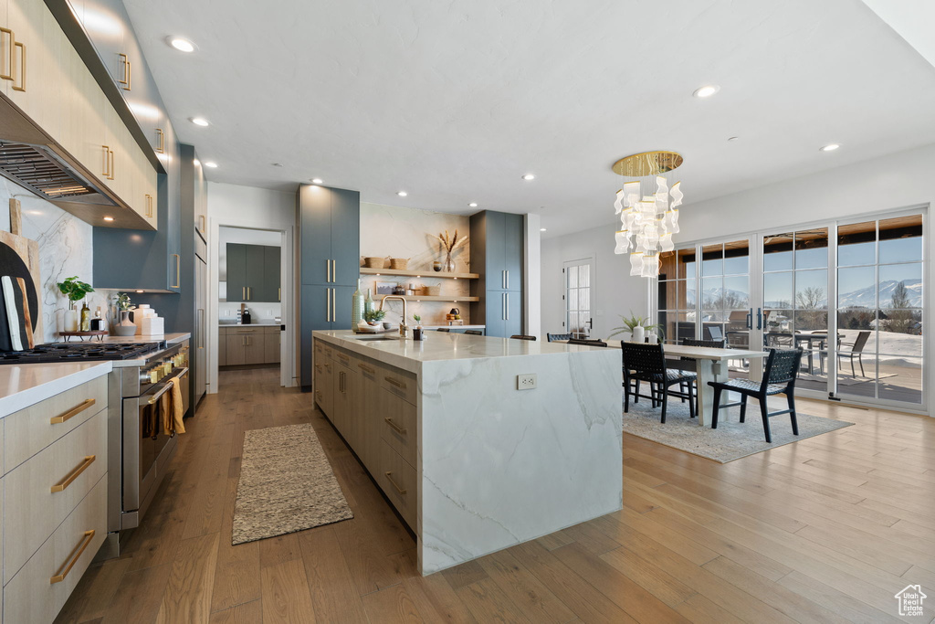 Kitchen with light hardwood / wood-style flooring, sink, a center island with sink, and stainless steel range