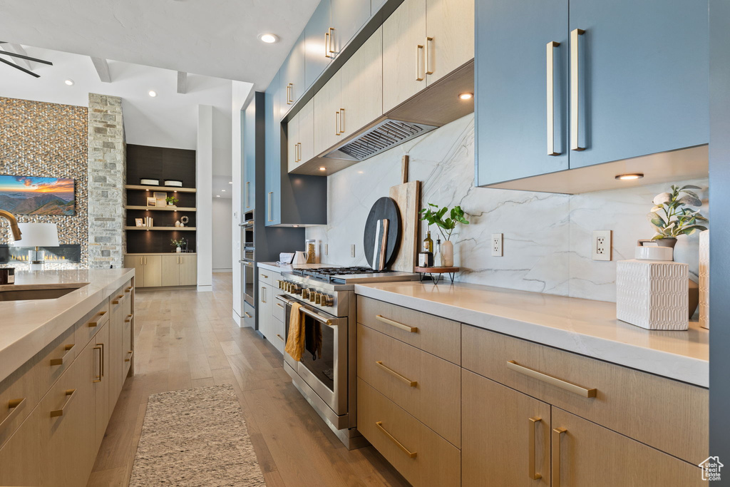 Kitchen featuring stainless steel appliances, backsplash, sink, ceiling fan, and light wood-type flooring