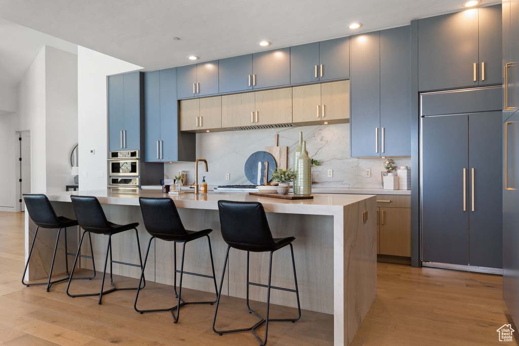 Kitchen with a breakfast bar area, light hardwood / wood-style floors, tasteful backsplash, and paneled fridge