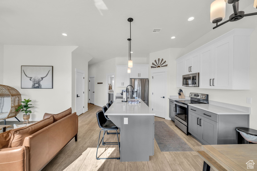Kitchen featuring appliances with stainless steel finishes, an island with sink, a breakfast bar, decorative light fixtures, and white cabinets
