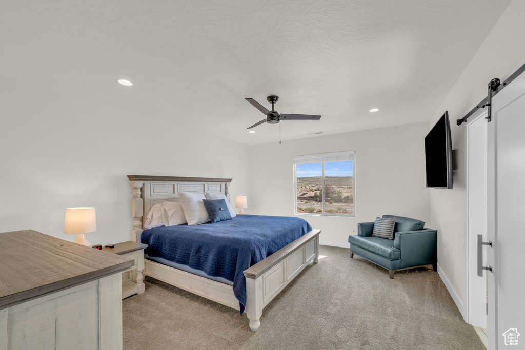 Bedroom featuring ceiling fan, light colored carpet, and a barn door