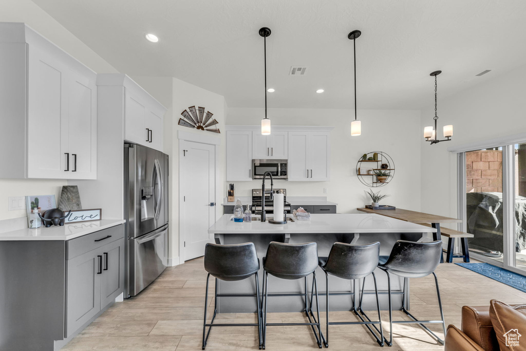 Kitchen featuring decorative light fixtures, a center island with sink, stainless steel appliances, and white cabinetry