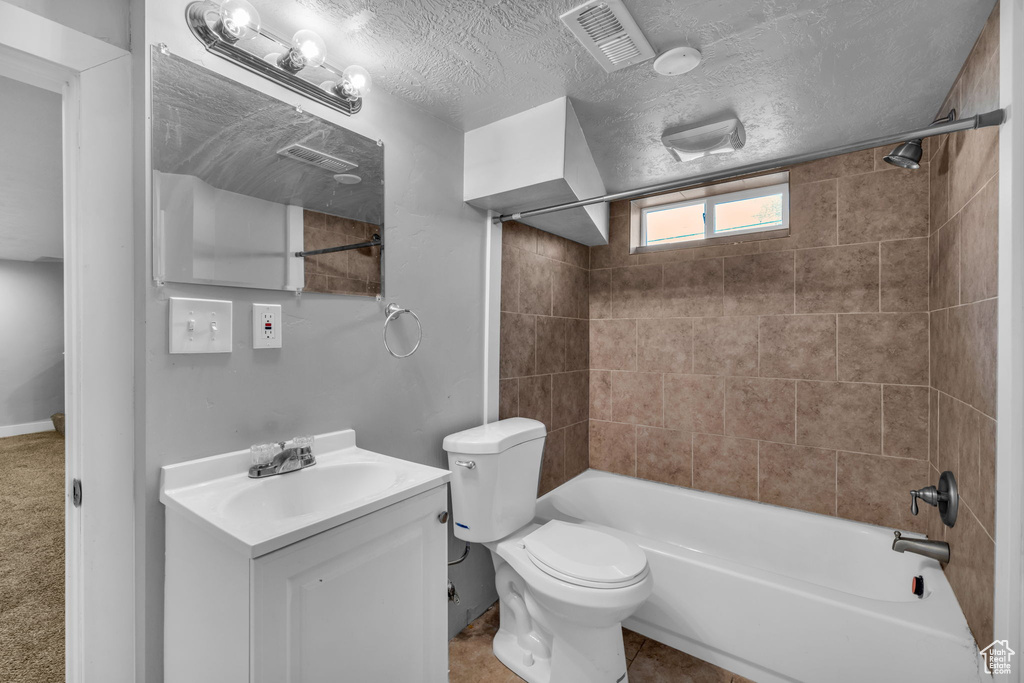 Full bathroom with toilet, tiled shower / bath, vanity with extensive cabinet space, a textured ceiling, and tile flooring