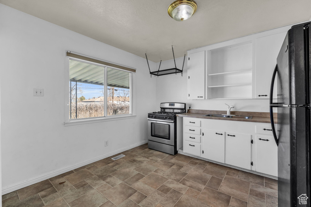 Kitchen featuring stainless steel gas range, white cabinets, sink, black refrigerator, and dark tile flooring