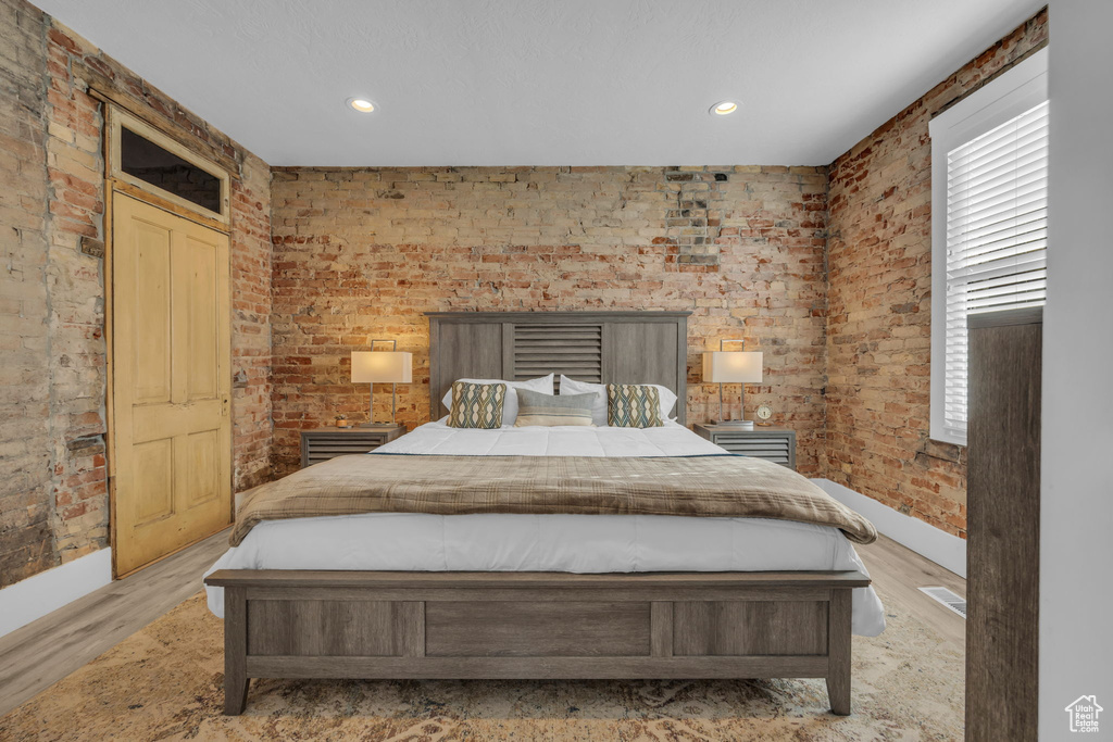 Bedroom with light hardwood / wood-style flooring and brick wall
