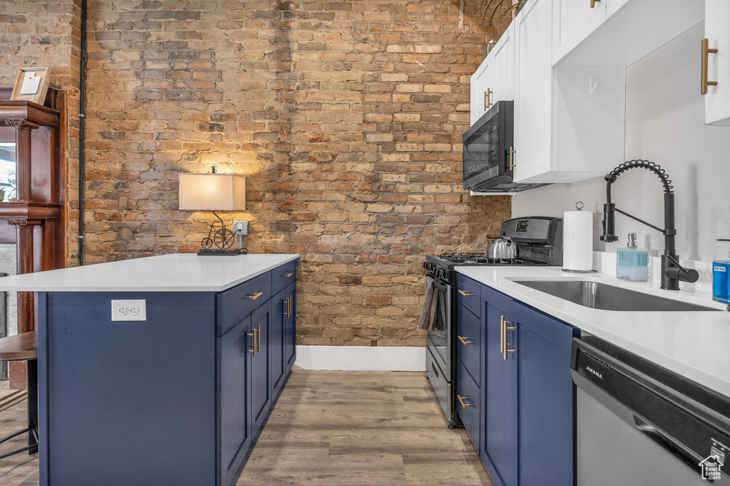 Kitchen with brick wall, light hardwood / wood-style floors, appliances with stainless steel finishes, and white cabinetry
