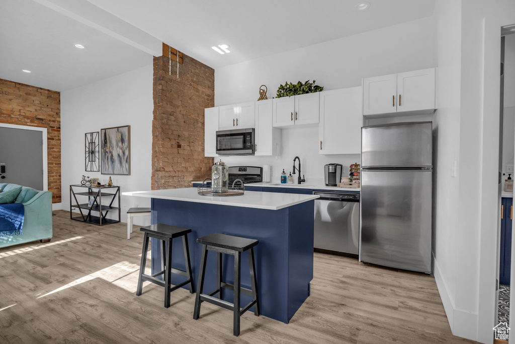 Kitchen featuring appliances with stainless steel finishes, a kitchen island, a kitchen bar, white cabinetry, and light hardwood / wood-style flooring
