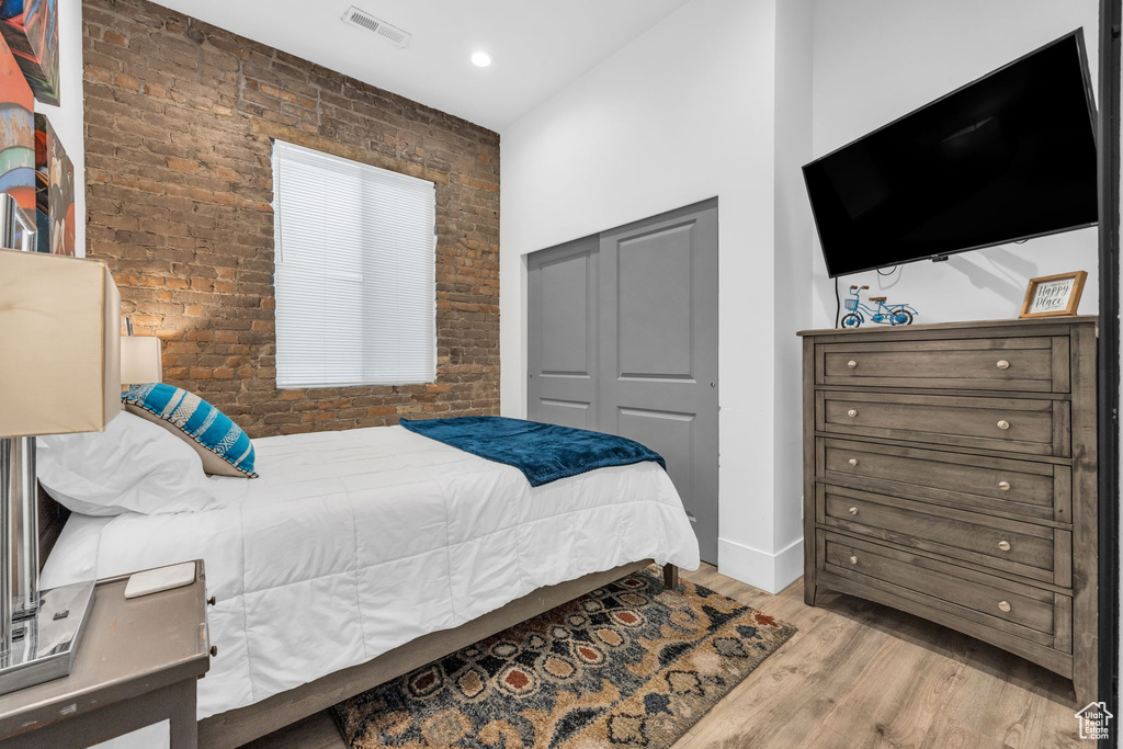 Bedroom featuring brick wall, a closet, and light hardwood / wood-style flooring