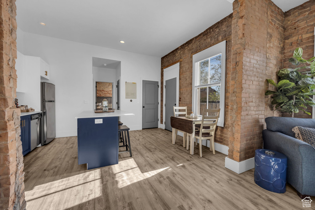 Interior space featuring brick wall, a breakfast bar, light hardwood / wood-style flooring, stainless steel appliances, and white cabinetry