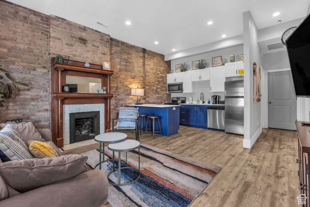 Living room featuring brick wall, a fireplace, sink, and light hardwood / wood-style flooring