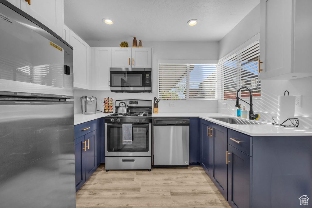 Kitchen featuring light hardwood / wood-style floors, white cabinetry, stainless steel appliances, blue cabinets, and sink