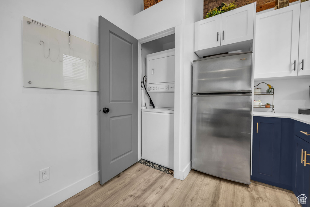 Kitchen featuring stainless steel fridge, white cabinetry, stacked washing maching and dryer, light hardwood / wood-style flooring, and blue cabinets