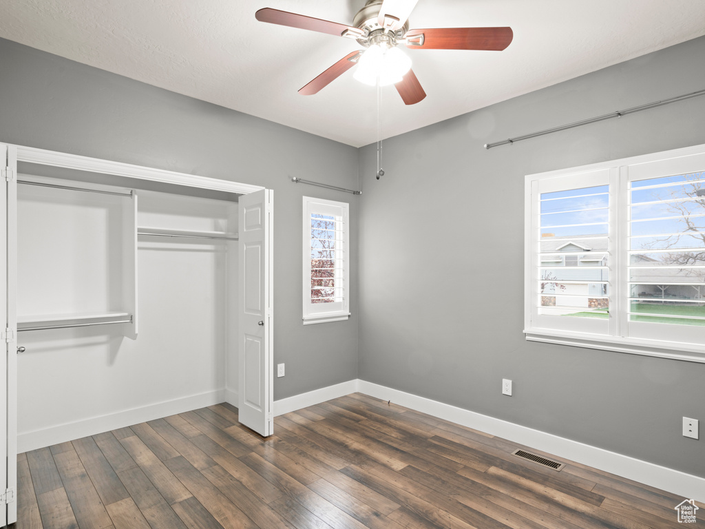 Unfurnished bedroom featuring a closet, ceiling fan, multiple windows, and dark wood-type flooring