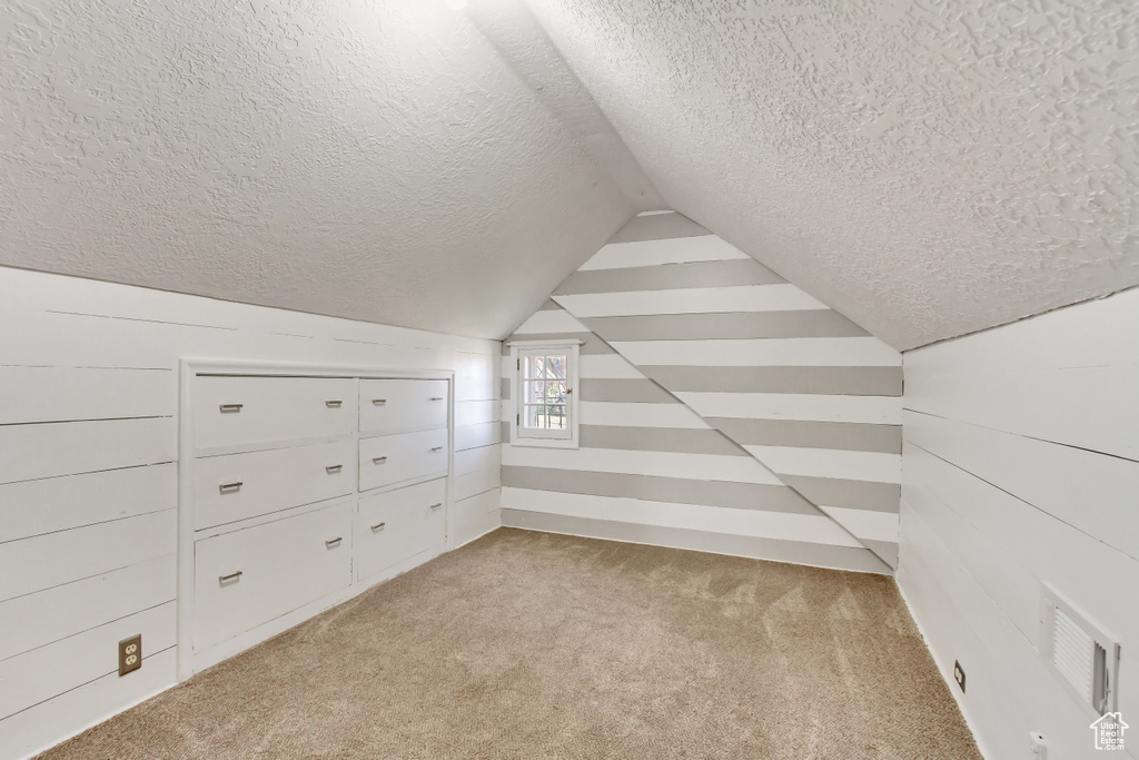 Additional living space with a textured ceiling, light colored carpet, and vaulted ceiling