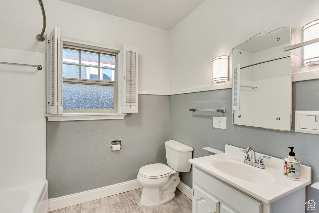 Full bathroom featuring toilet, hardwood / wood-style flooring, washtub / shower combination, tile walls, and vanity