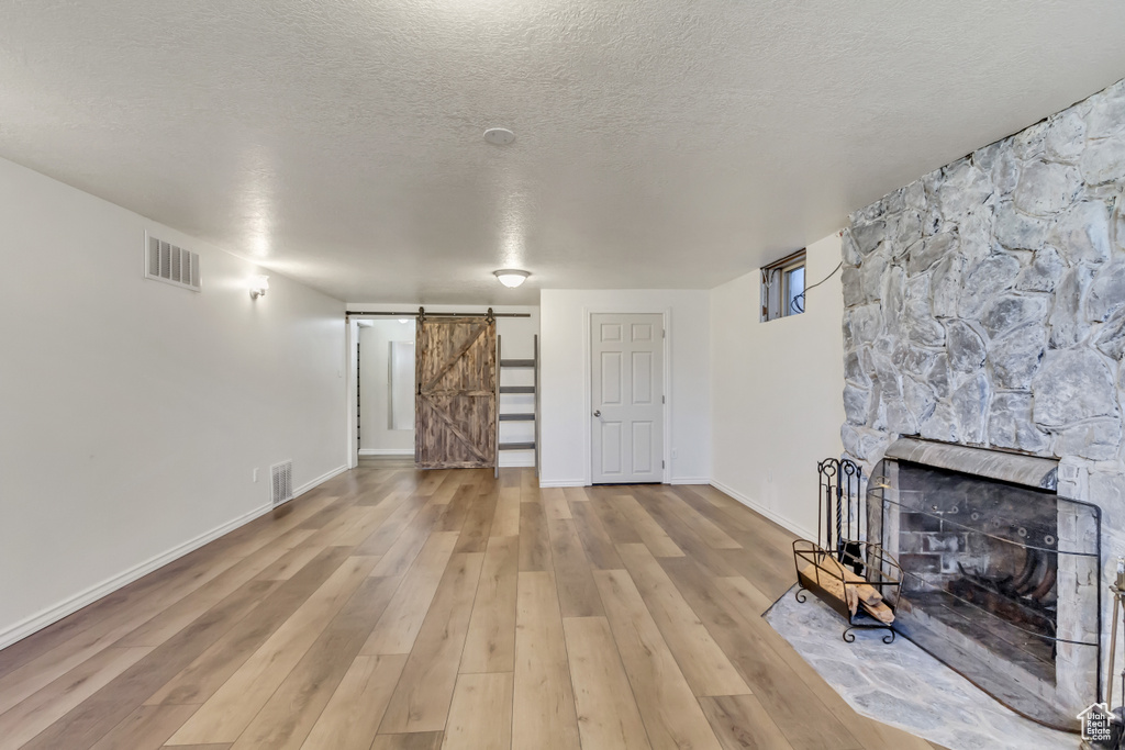 Unfurnished living room featuring a barn door, a fireplace, a textured ceiling, and light hardwood / wood-style floors