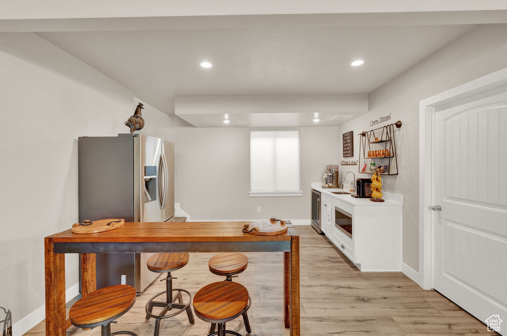 Kitchen featuring white cabinetry, wine cooler, refrigerator, light hardwood / wood-style flooring, and sink