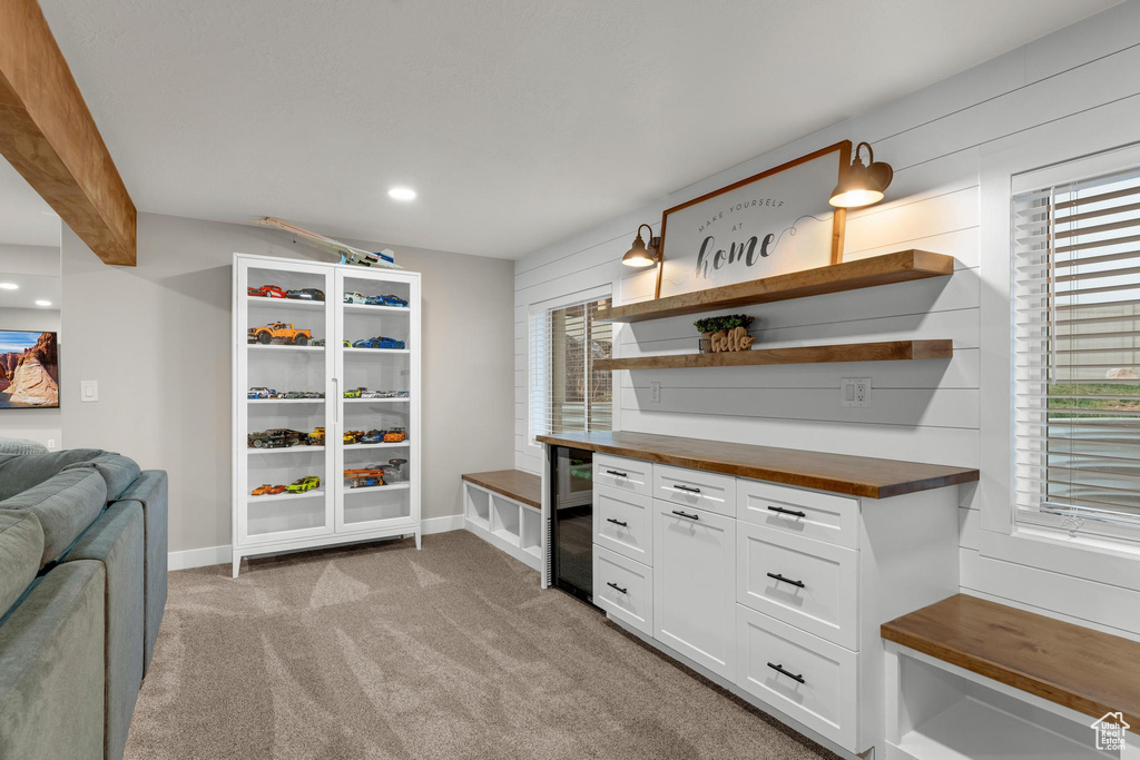 Interior space featuring light carpet, wooden counters, white cabinetry, and beamed ceiling