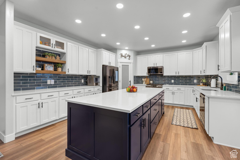 Kitchen with light hardwood / wood-style floors, white cabinets, backsplash, and stainless steel appliances