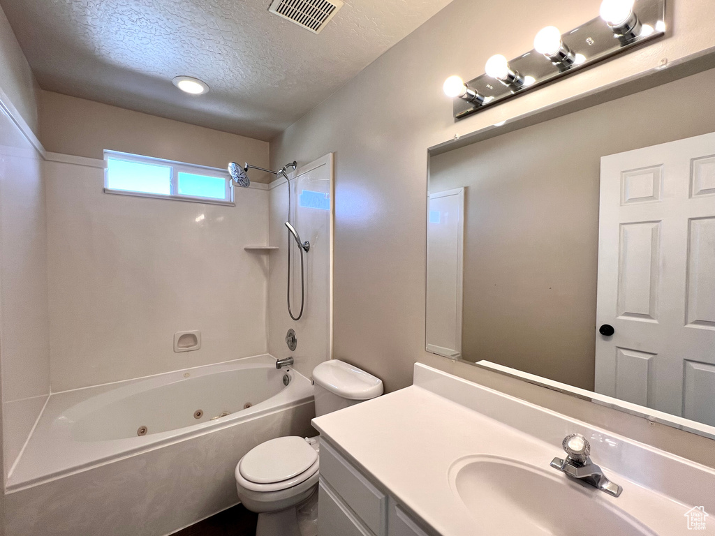 Full bathroom with a textured ceiling, toilet, vanity, and shower / tub combination