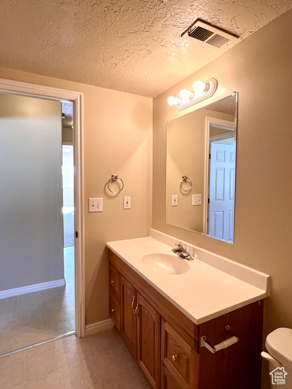 Bathroom featuring tile floors, toilet, large vanity, and a textured ceiling