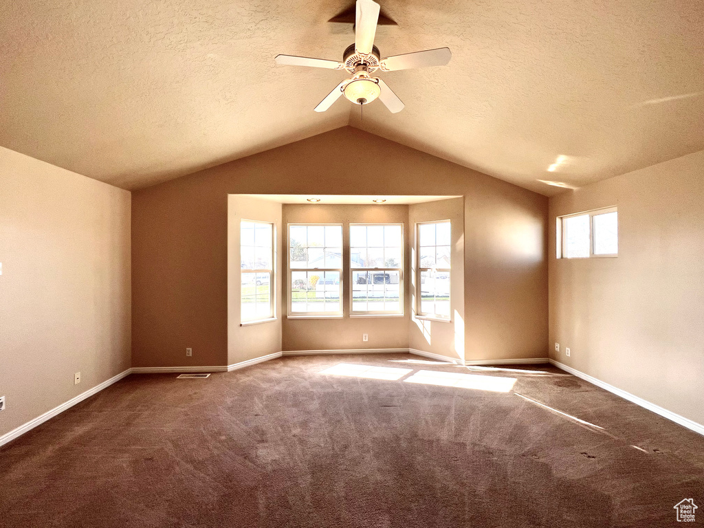 Spare room featuring vaulted ceiling, a textured ceiling, ceiling fan, and dark colored carpet