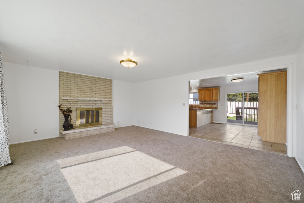 Unfurnished living room with brick wall, light colored carpet, and a fireplace
