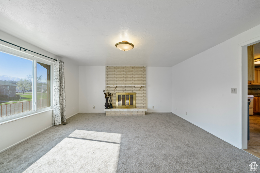 Unfurnished living room with light colored carpet, brick wall, and a brick fireplace