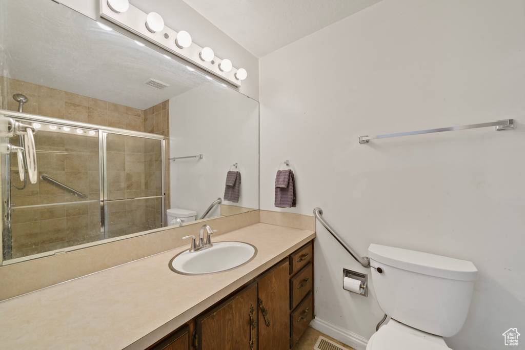 Bathroom featuring large vanity, a shower with shower door, and toilet