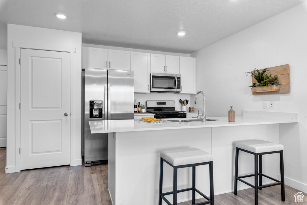 Kitchen with appliances with stainless steel finishes, sink, a breakfast bar, light hardwood / wood-style flooring, and white cabinetry