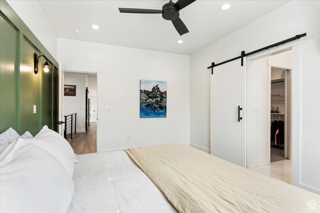 Bedroom with a spacious closet, a barn door, light carpet, ceiling fan, and a closet