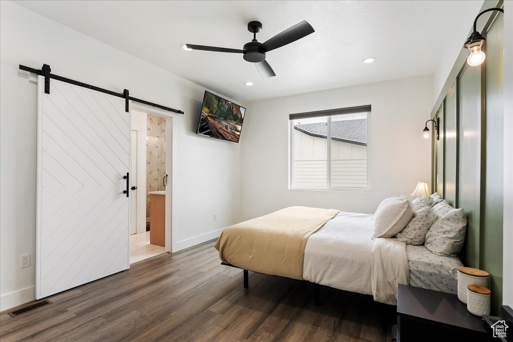 Bedroom with a barn door, ceiling fan, dark hardwood / wood-style floors, and ensuite bath