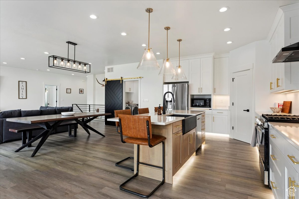 Kitchen with an island with sink, stainless steel appliances, dark hardwood / wood-style flooring, a kitchen breakfast bar, and a barn door