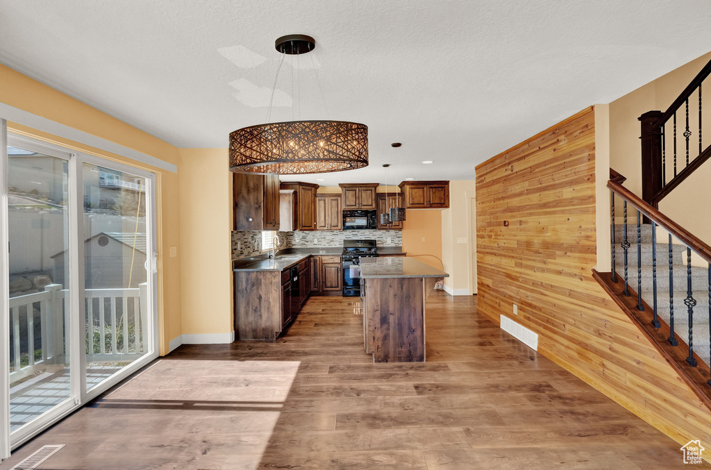 Kitchen with wood walls, range, a kitchen island, light wood-type flooring, and hanging light fixtures