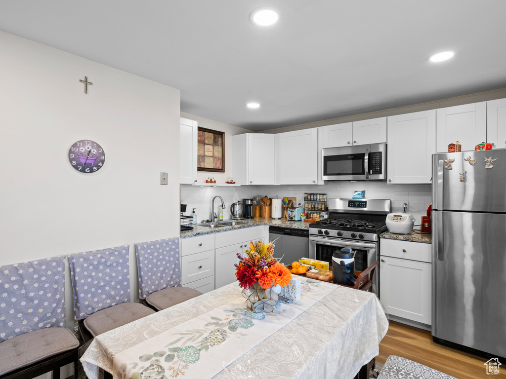 Kitchen featuring white cabinets, light hardwood / wood-style flooring, tasteful backsplash, and stainless steel appliances
