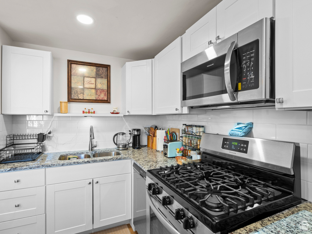 Kitchen featuring appliances with stainless steel finishes, backsplash, white cabinets, and sink