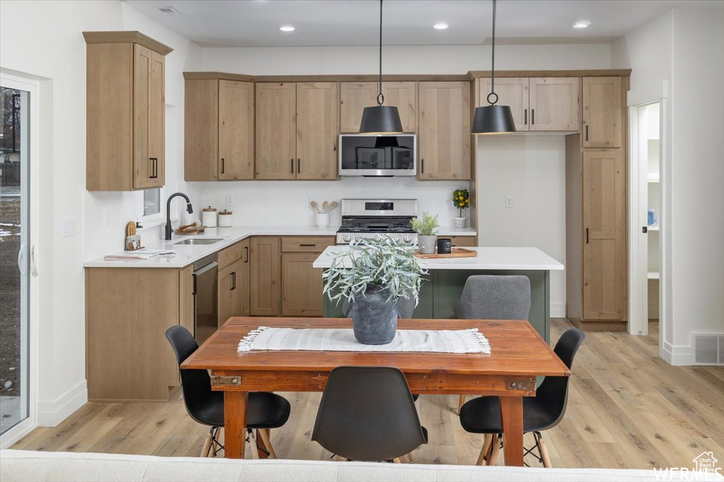 Kitchen with appliances with stainless steel finishes, sink, pendant lighting, and light hardwood / wood-style flooring