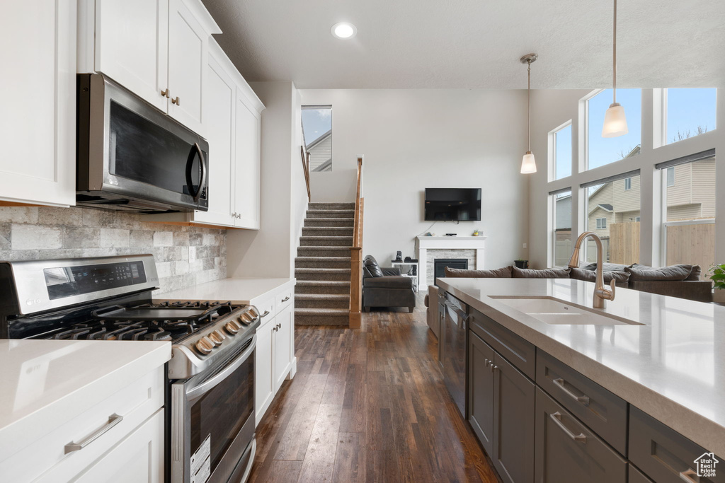 Kitchen with pendant lighting, stainless steel appliances, backsplash, white cabinetry, and dark hardwood / wood-style floors