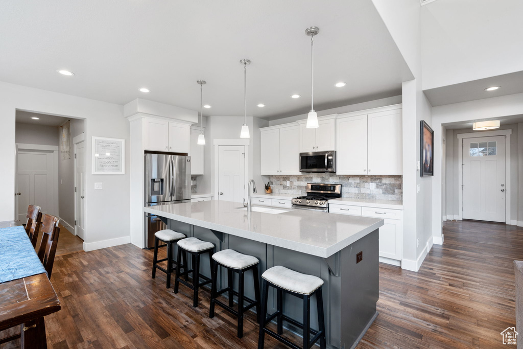 Kitchen featuring stainless steel appliances, white cabinets, dark hardwood / wood-style flooring, an island with sink, and decorative light fixtures