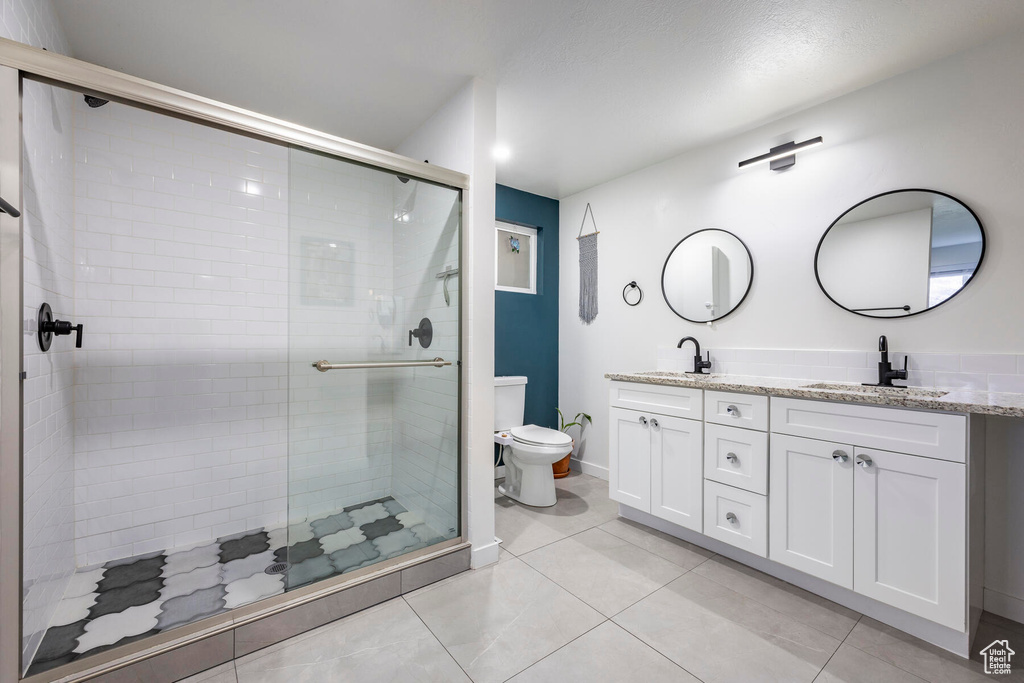 Bathroom with double vanity, tile floors, a shower with shower door, and toilet