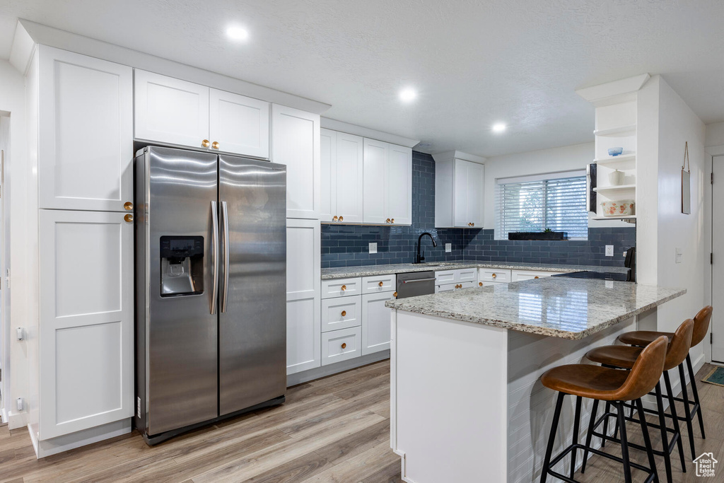 Kitchen featuring appliances with stainless steel finishes, light wood-type flooring, backsplash, light stone countertops, and white cabinets