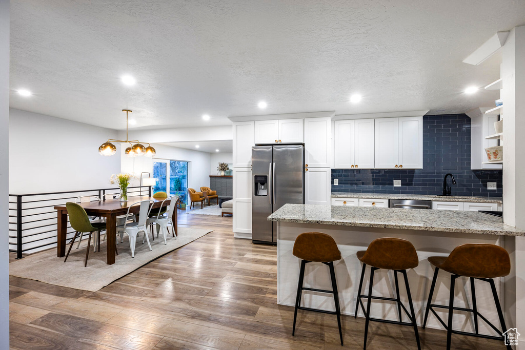 Kitchen with appliances with stainless steel finishes, hanging light fixtures, backsplash, a chandelier, and light hardwood / wood-style flooring