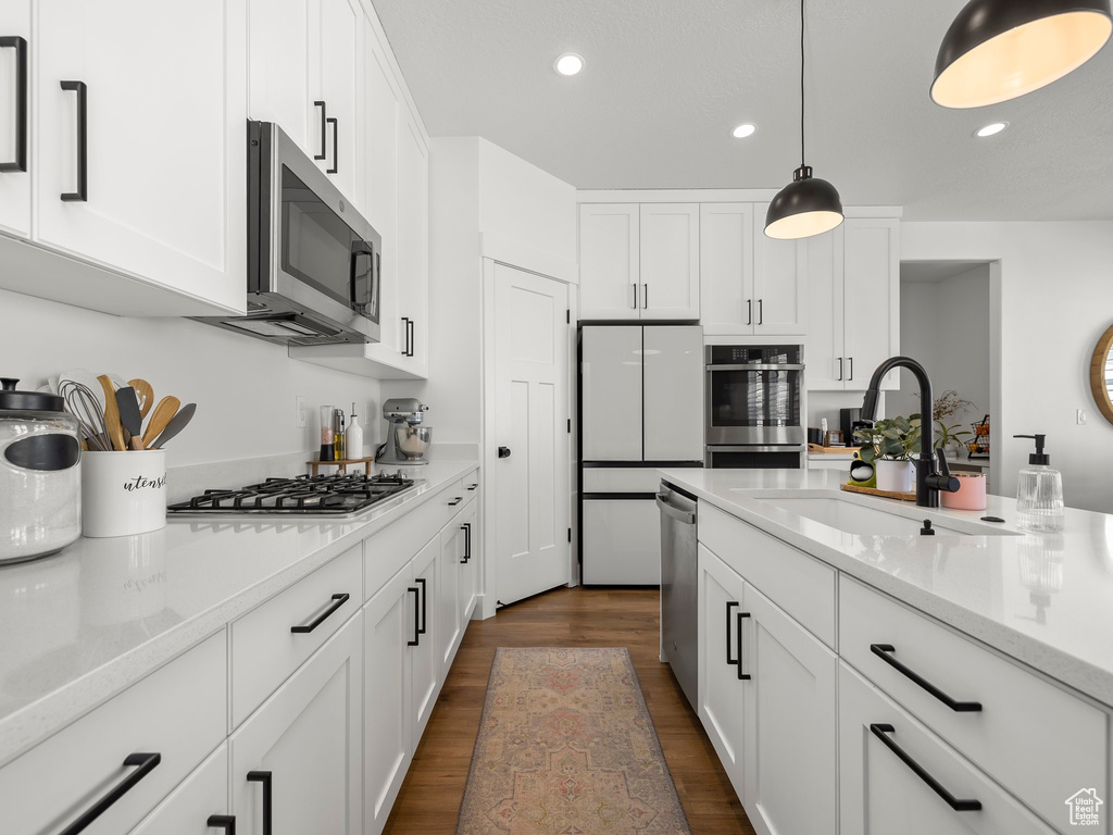 Kitchen featuring pendant lighting, stainless steel appliances, sink, white cabinetry, and dark hardwood / wood-style floors