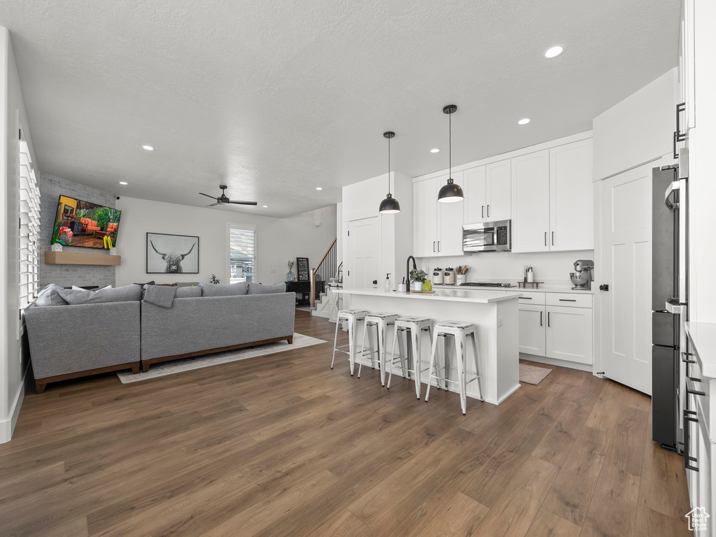 Kitchen with appliances with stainless steel finishes, ceiling fan, decorative light fixtures, dark hardwood / wood-style flooring, and white cabinets